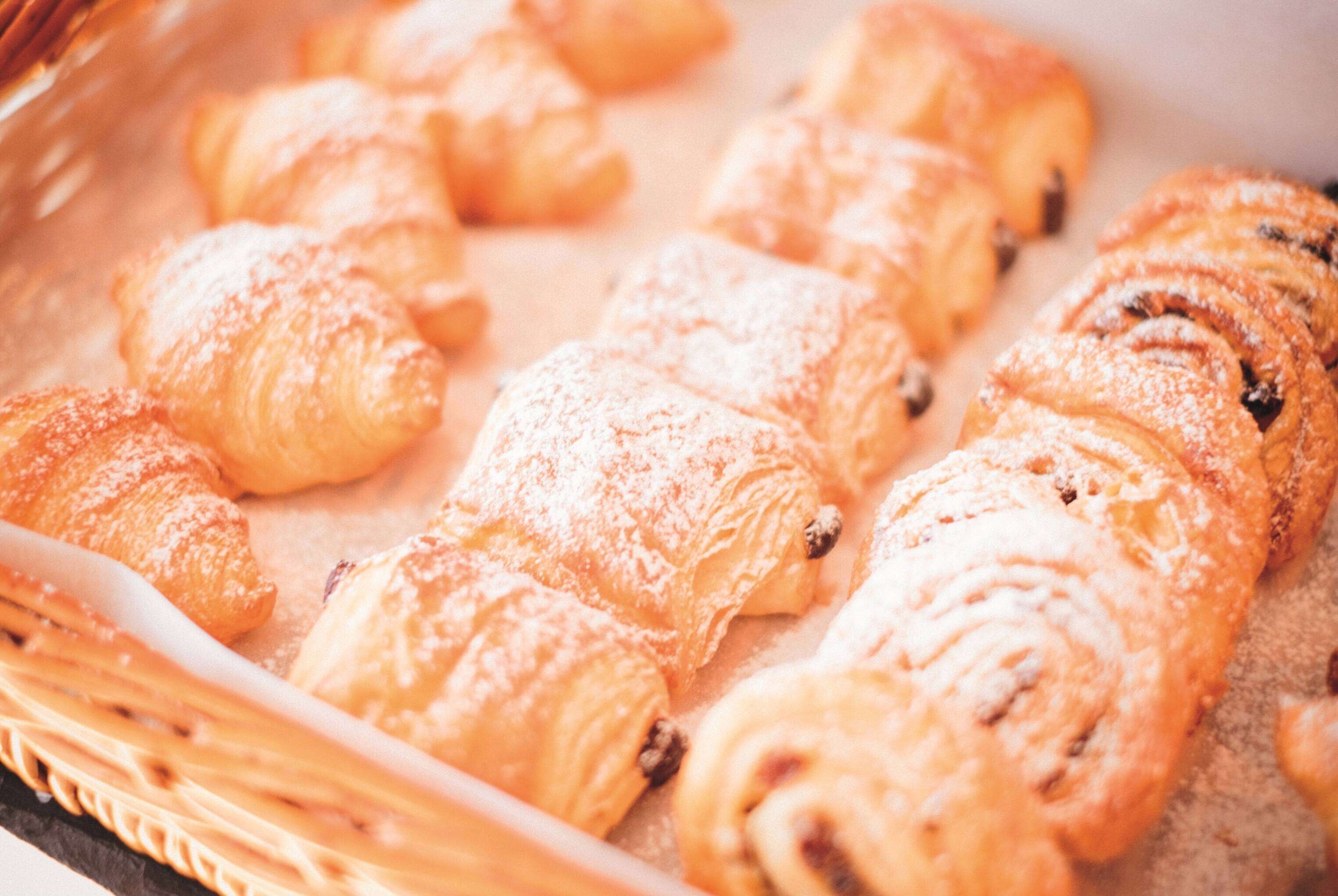 A tray of assorted pastries, including croissants and a cinnamon roll, dusted with powdered sugar.