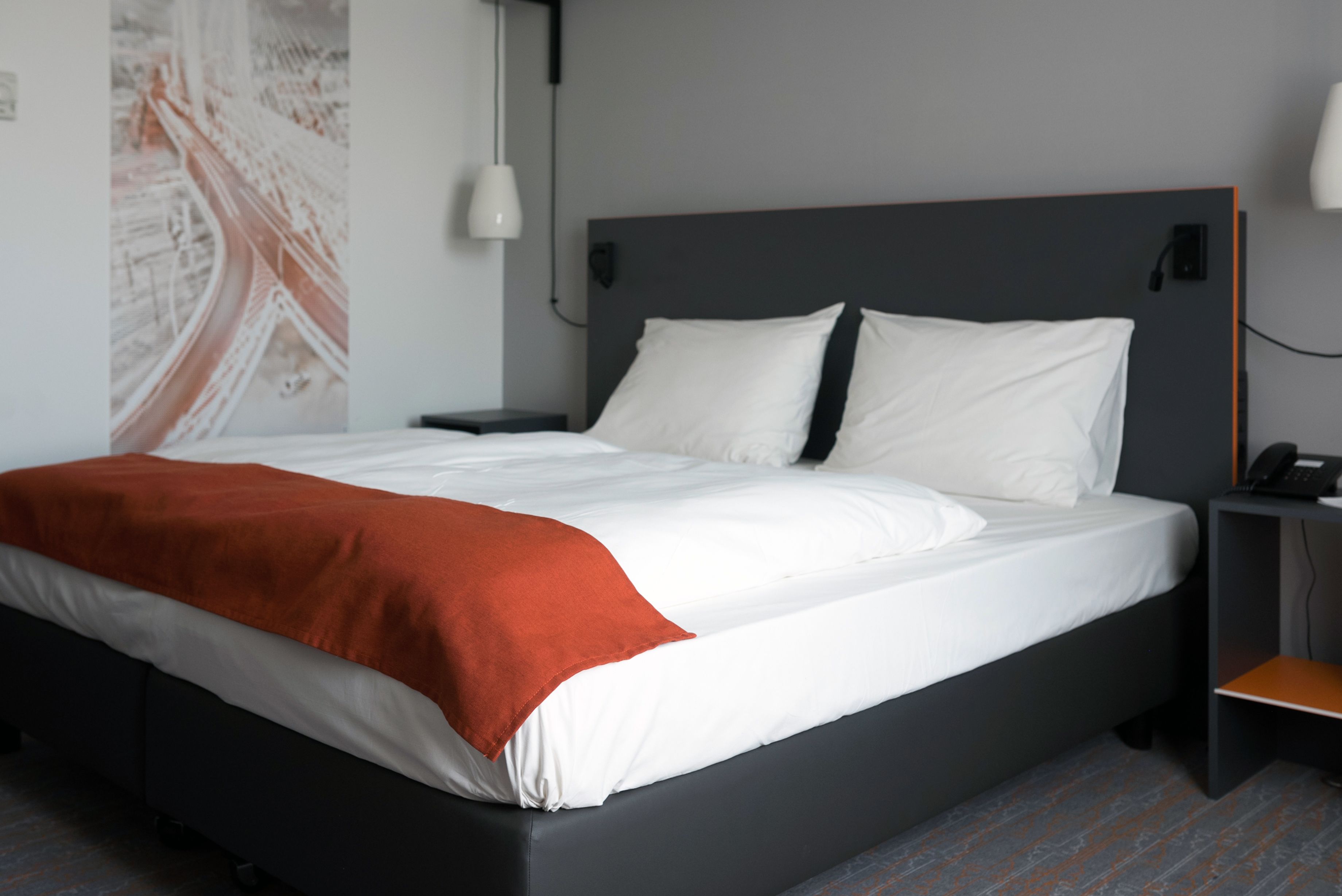 A modern hotel room with a large bed, a nightstand, a wall-mounted lamp, and a telephone.