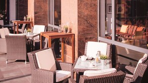 Un espace extérieur aménagé avec des meubles en osier et une table en verre, offrant une vue dégagée grâce à de grandes fenêtres.