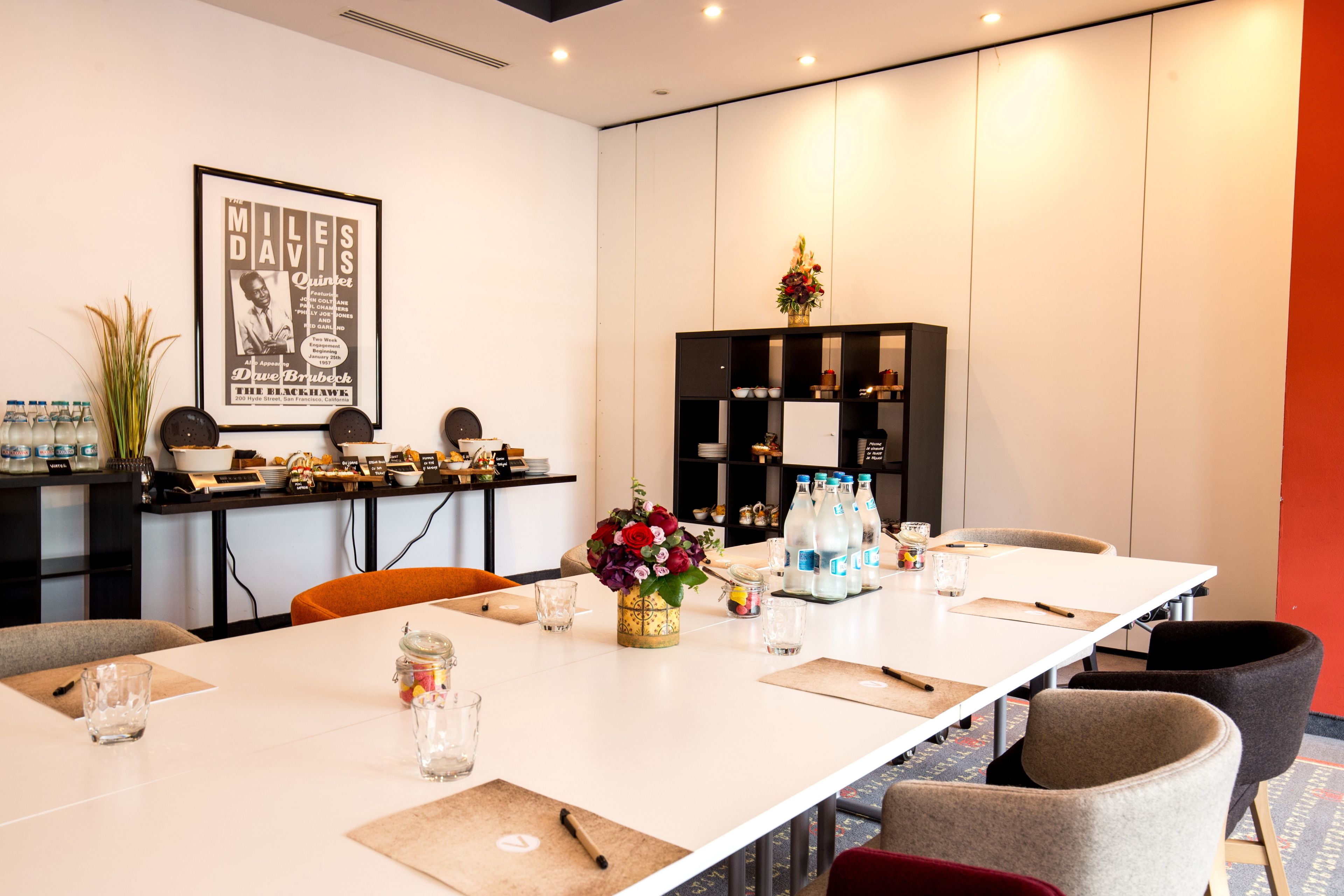 A conference room with a long table, chairs, a bookshelf, and a framed poster on the wall.
