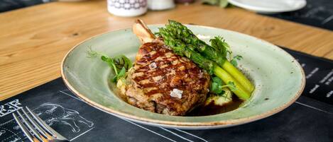 A plate with a grilled meat, asparagus, and a sauce on a table with a black placemat.