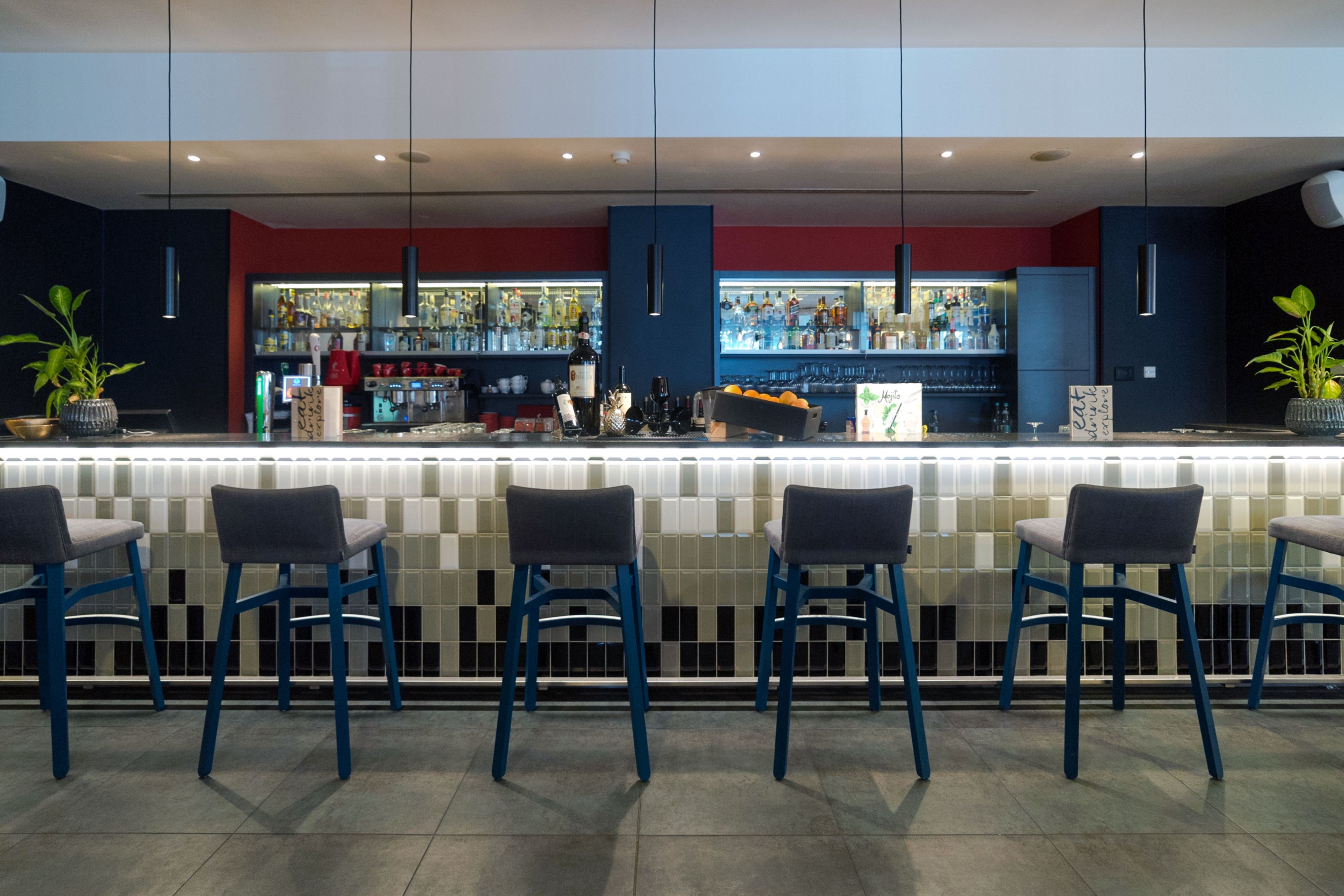 Un espace bar agrémenté d’un mur recouvert de carreaux, de tabourets de bar bleus et d’un comptoir bien garni.