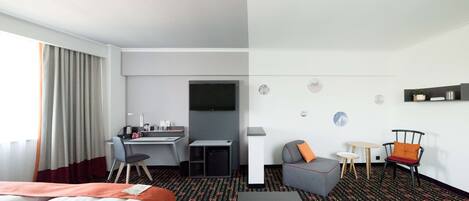A hotel room with a bed, desk, two chairs, a small table, and a sofa.