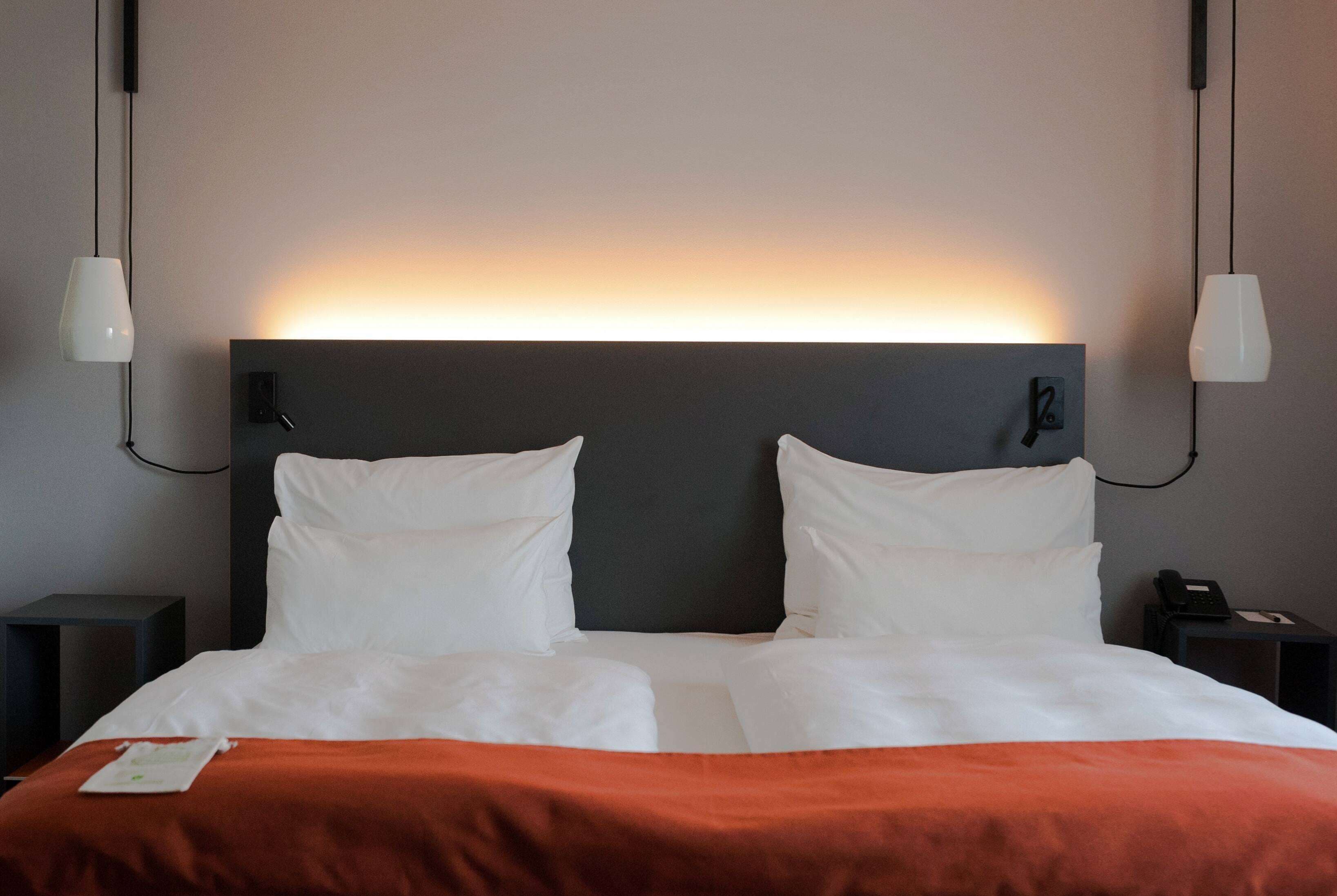 A hotel room with a large bed, white bedding, a dark headboard, and two bedside lamps.