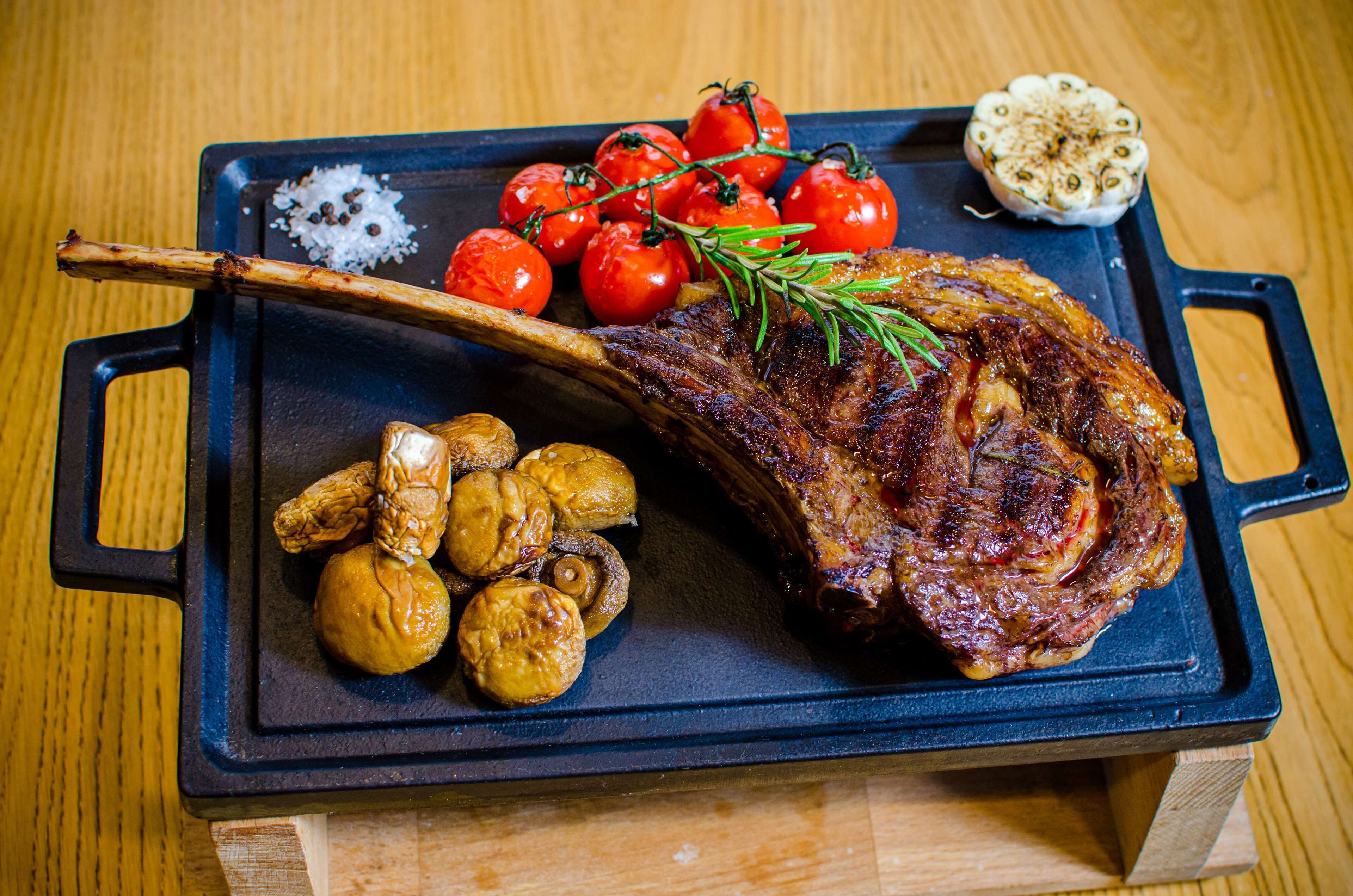 Un steak grillé, accompagné de pommes de terre rôties et de tomates cerises, servi sur un plateau noir.