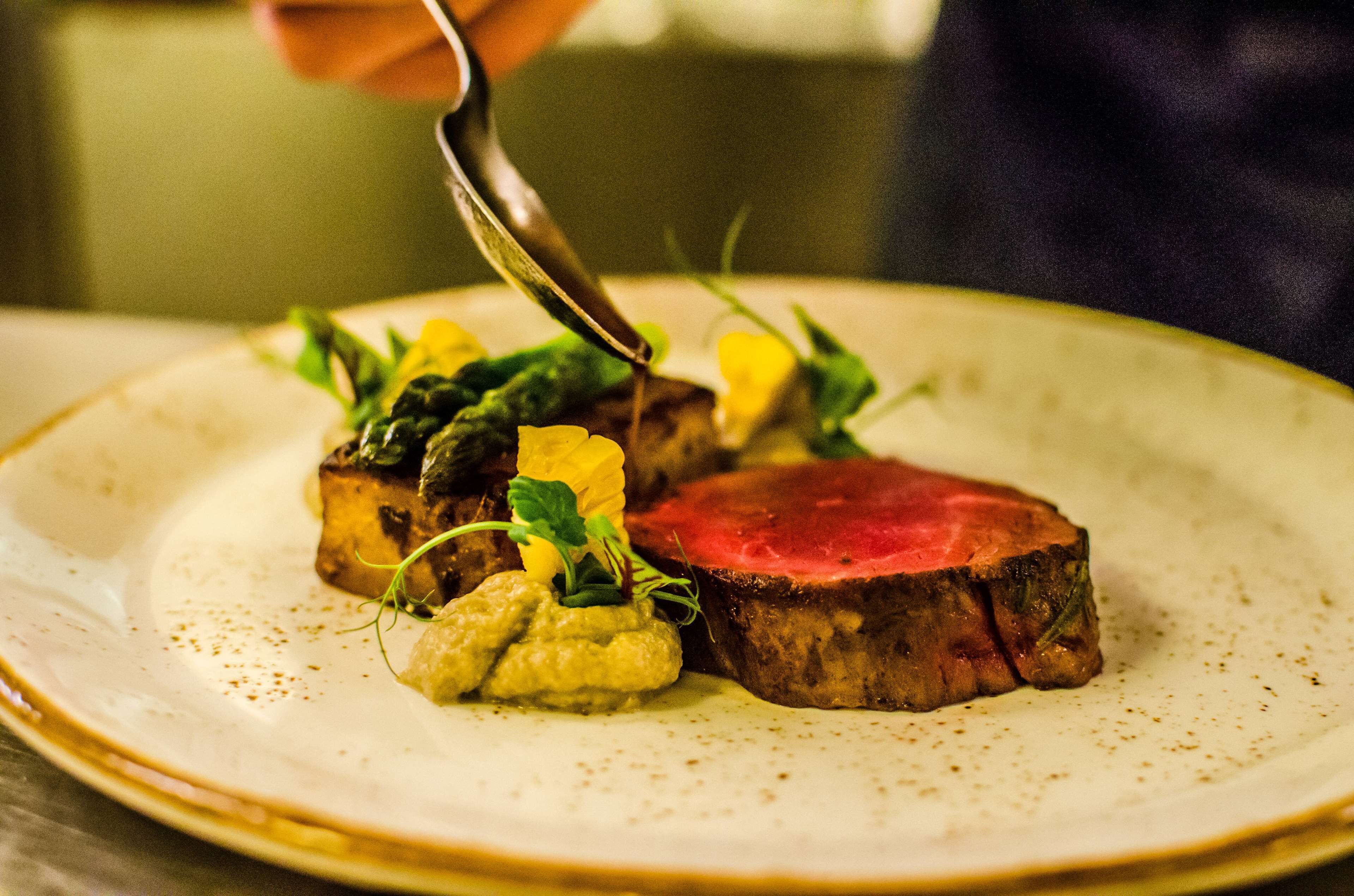 A plate with a steak, vegetables, and a sauce.