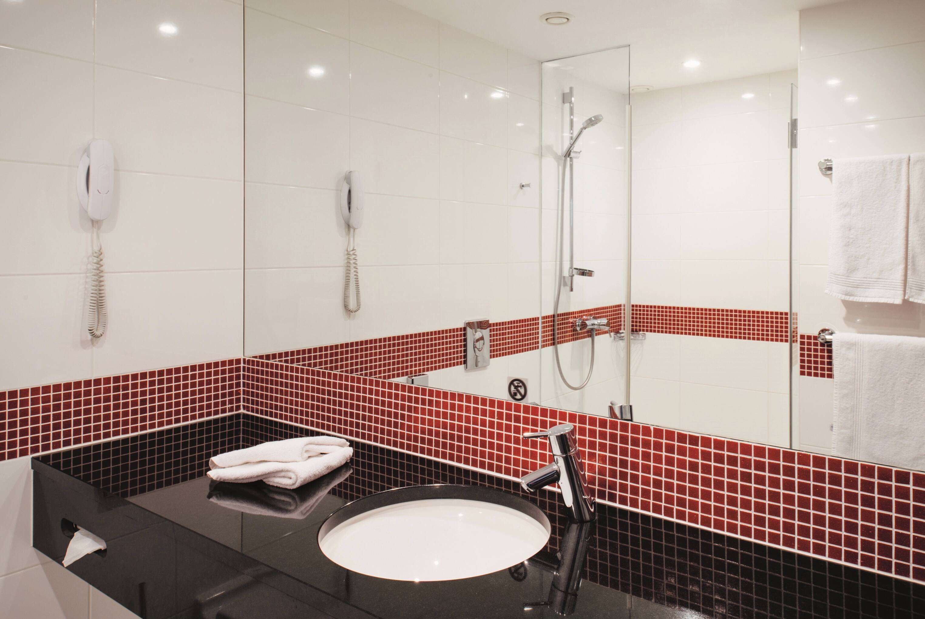 Uma casa de banho moderna com bancada preta, lavatório branco e paredes com azulejos vermelhos.
