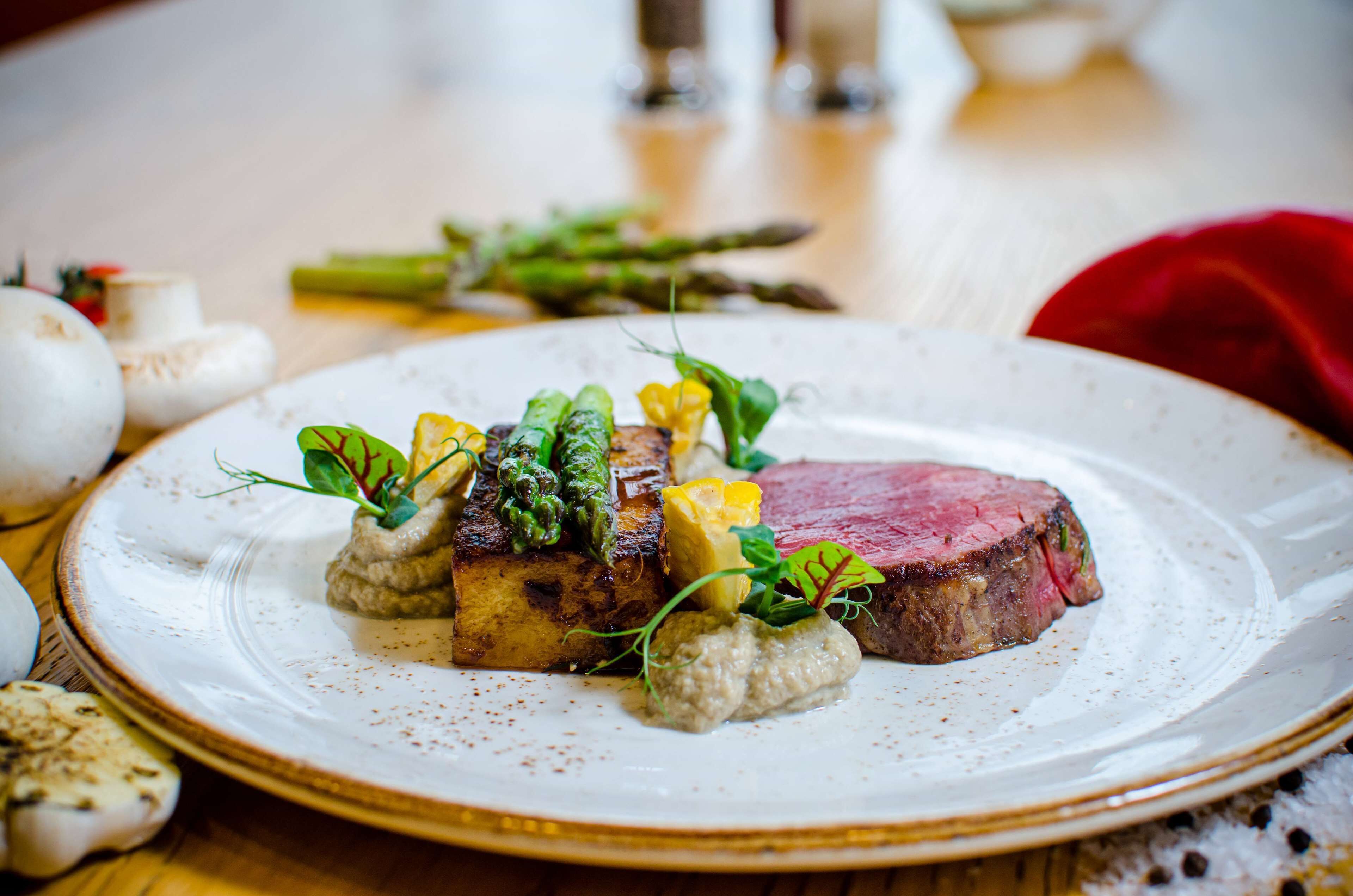 A plate of food with a steak, vegetables, and a creamy sauce.