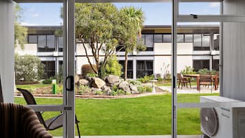 A view through a glass door of a building with a grassy courtyard, a tree, and outdoor furniture.