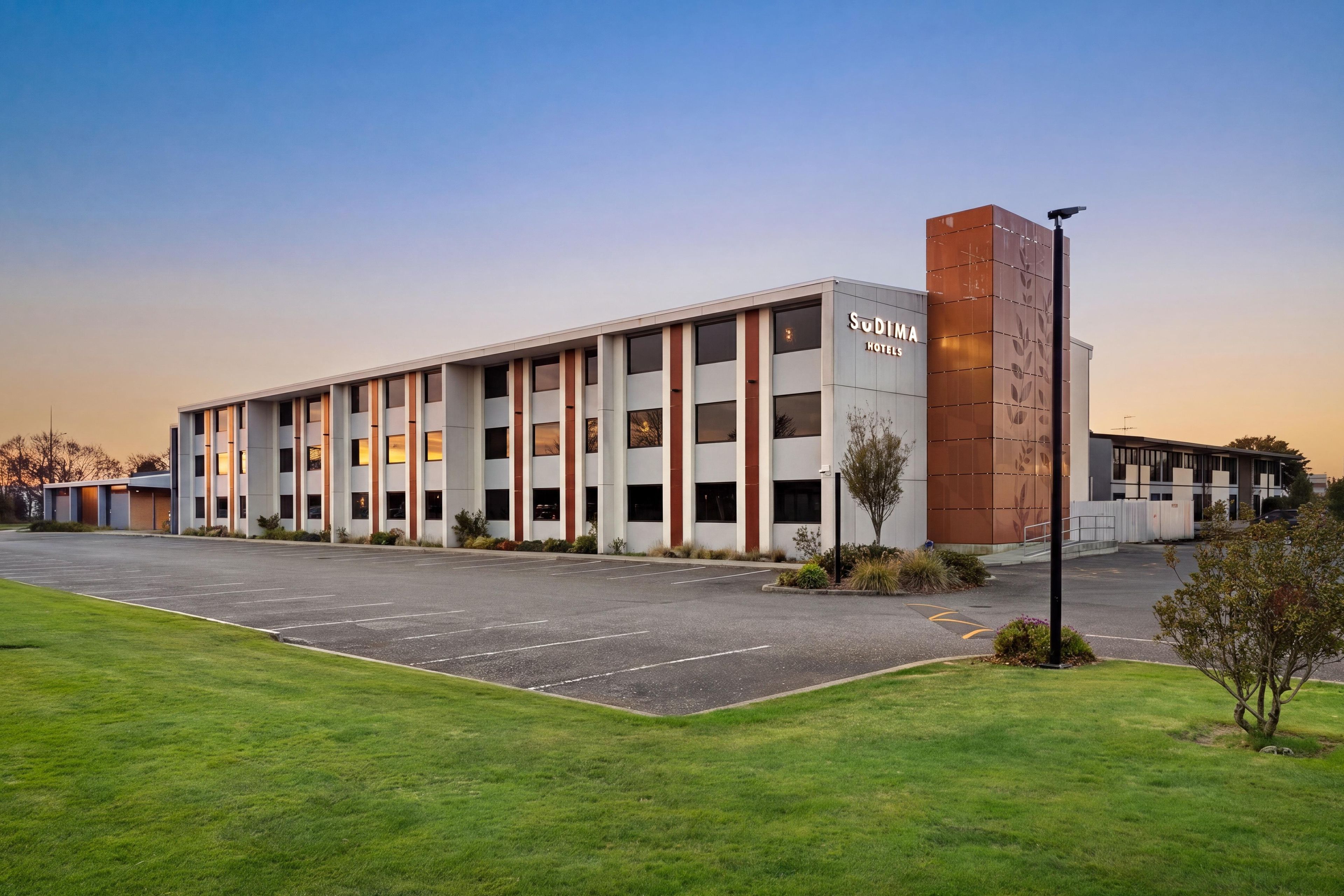 Een modern hotelgebouw met een parkeerplaats en een verzorgd gazon.