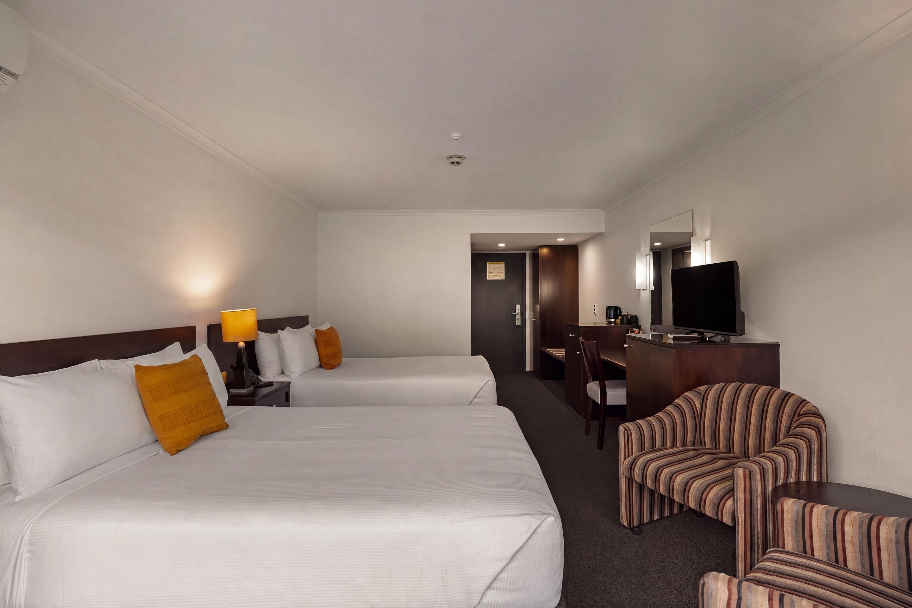 A hotel room with two beds, a desk with a TV, a chair, and a small table.