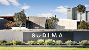 Entrada moderna de un hotel con un cartel grande que dice 'Sudima Hotels'.