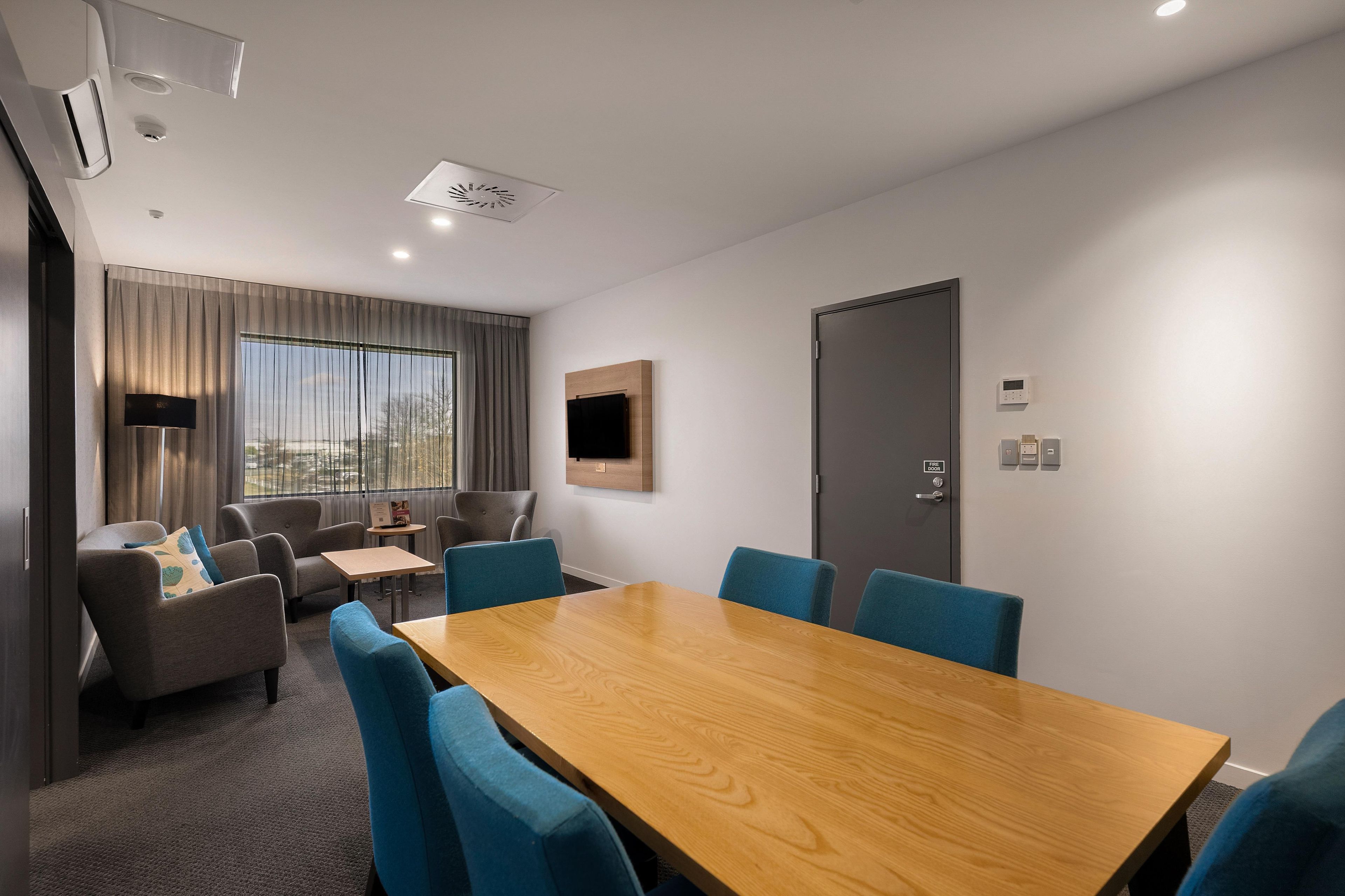 A conference room with a wooden table, blue chairs, a sofa, and a television.