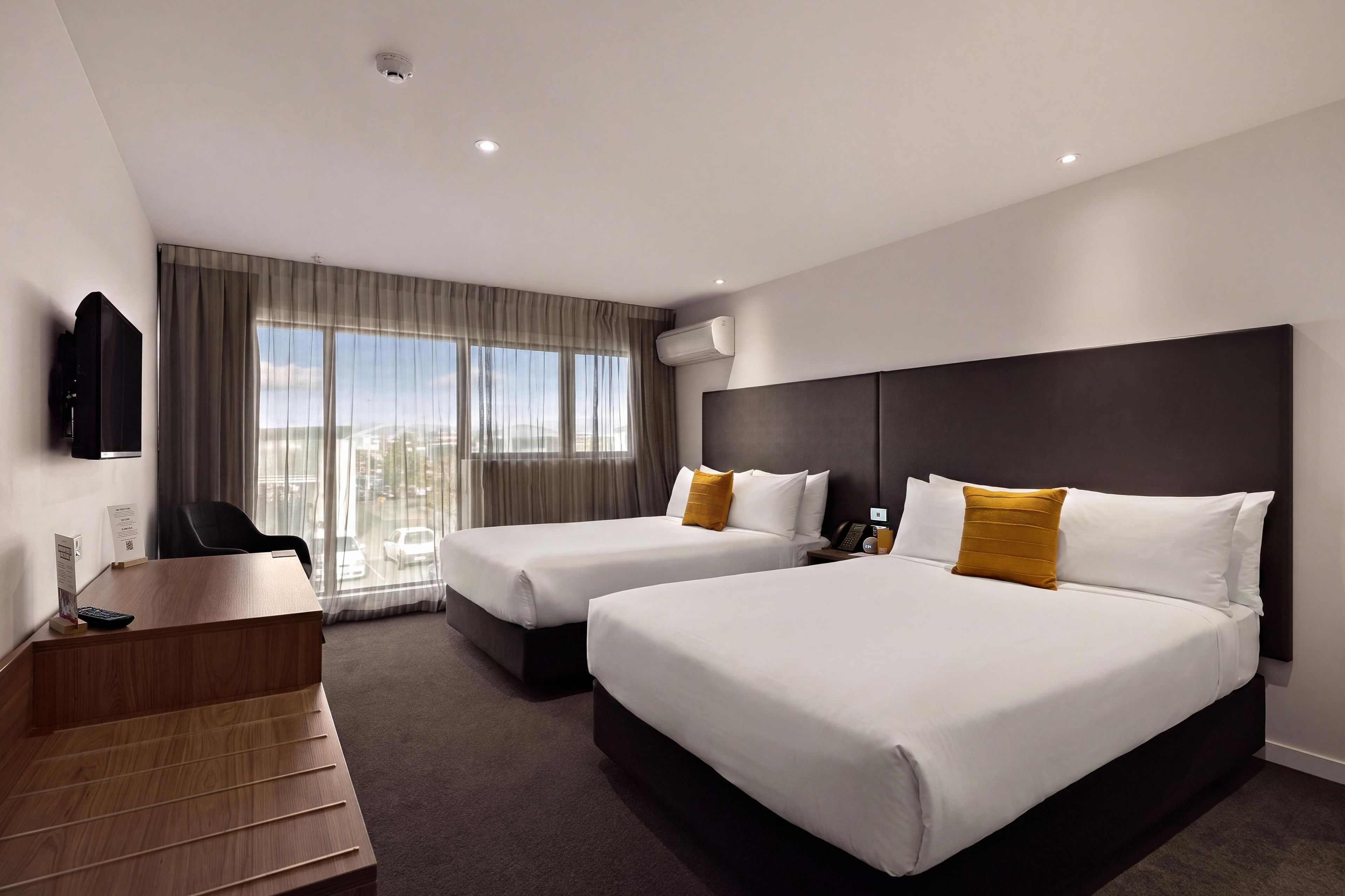 A hotel room with two beds, a desk, a chair, and a TV.