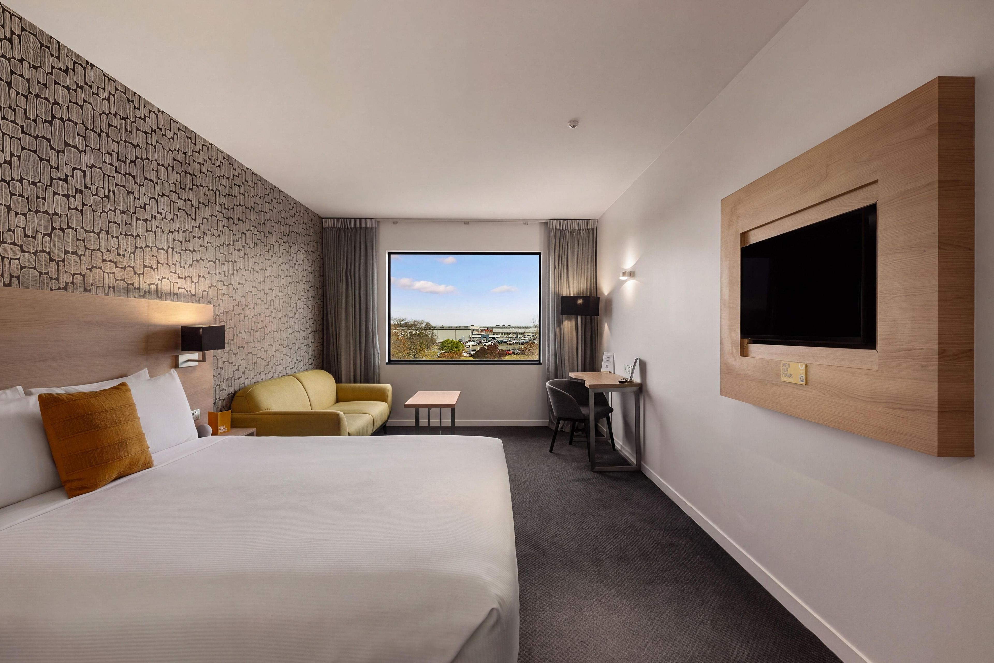 A hotel room with a large bed, a sofa, a desk, and a TV mounted on the wall.