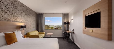 Habitación de hotel con una cama grande, un sofá, un escritorio y un televisor montado en la pared.