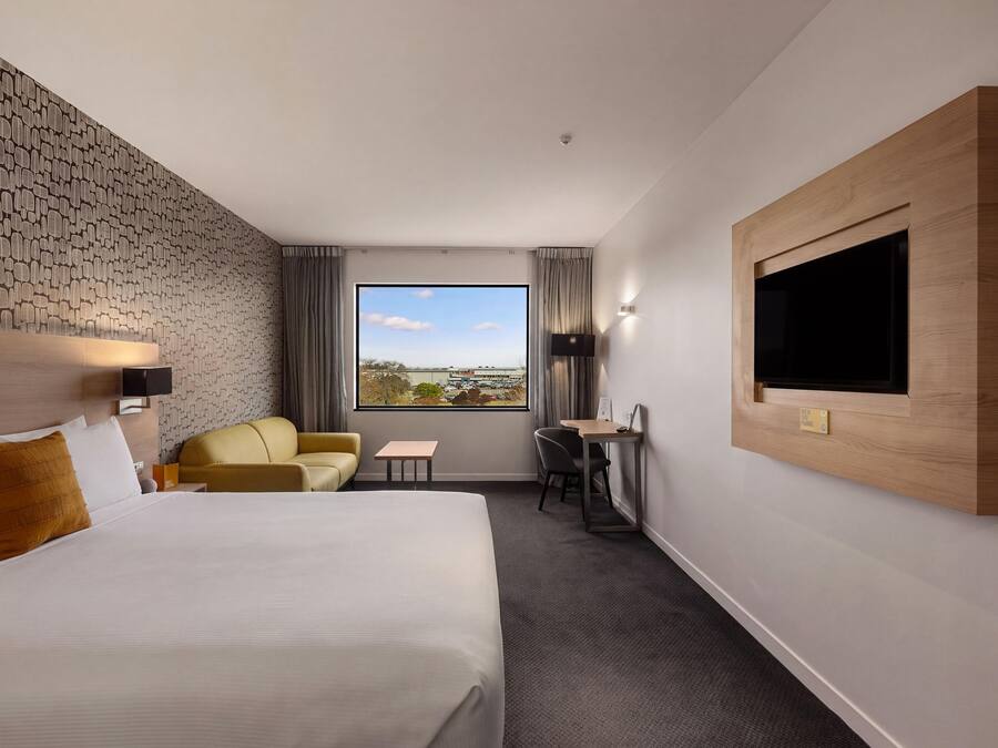 A hotel room with a large bed, a sofa, a desk, and a TV mounted on the wall.