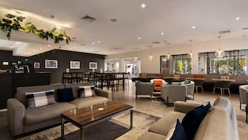 A spacious lobby with a sofa, chairs, a coffee table, and a dining area with tables and chairs.
