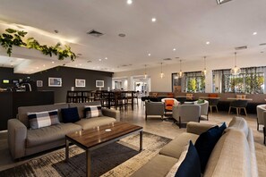 A spacious lobby with a sofa, chairs, a coffee table, and a dining area with tables and chairs. - Sudima Christchurch Airport (Christchurch)