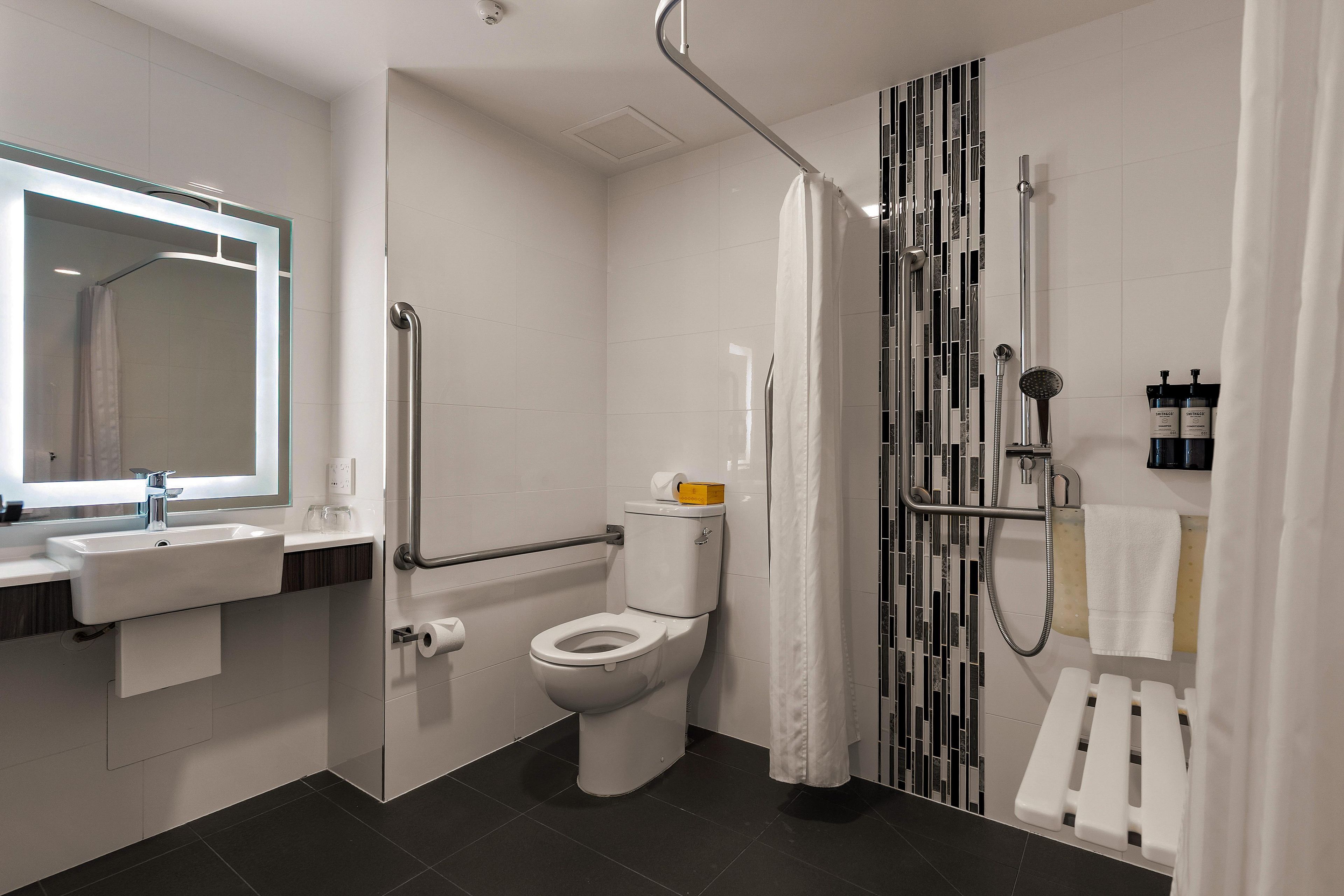 A modern bathroom with a toilet, sink, shower, and handrails.