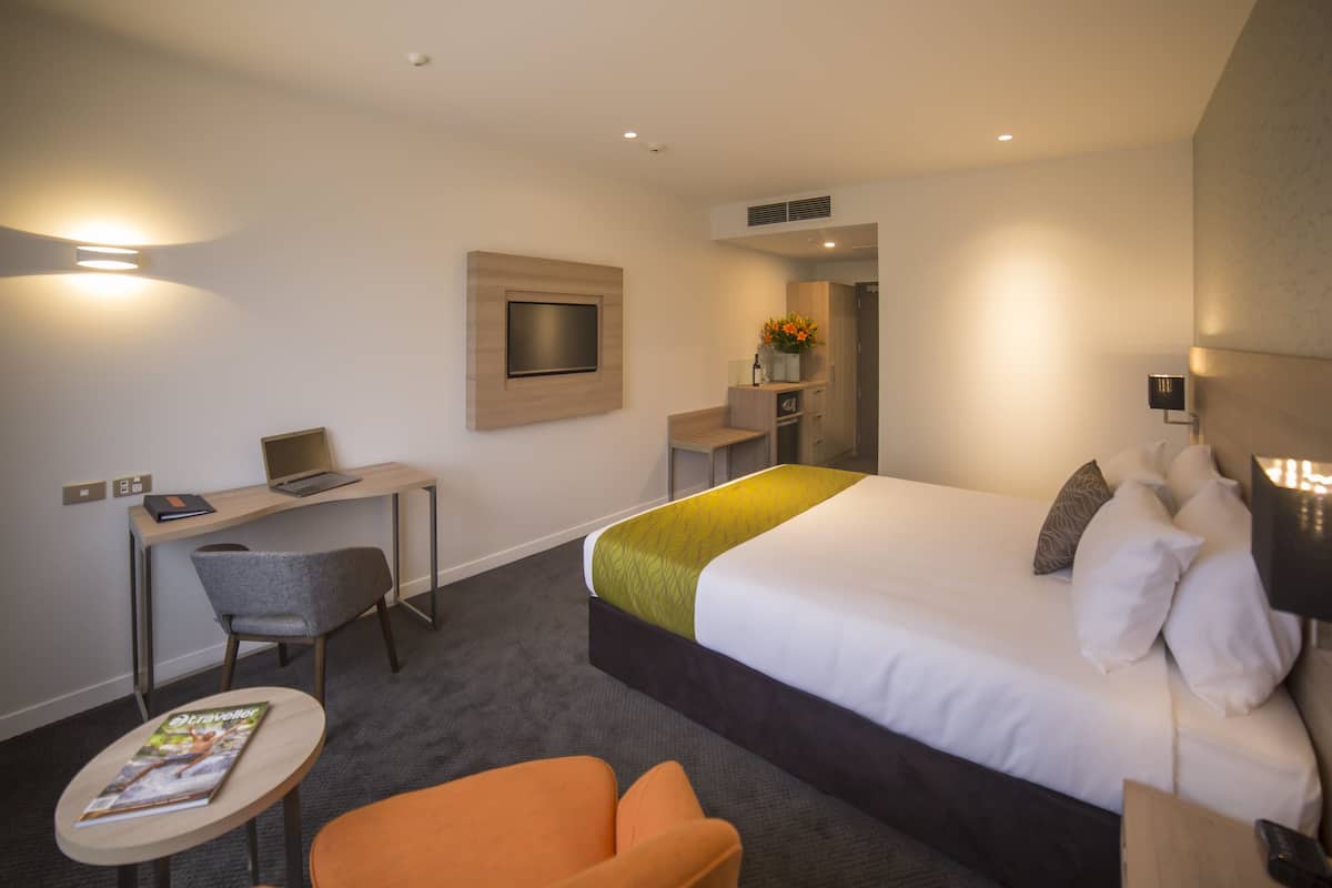 A hotel room with a bed, a desk, a chair, and a small table.