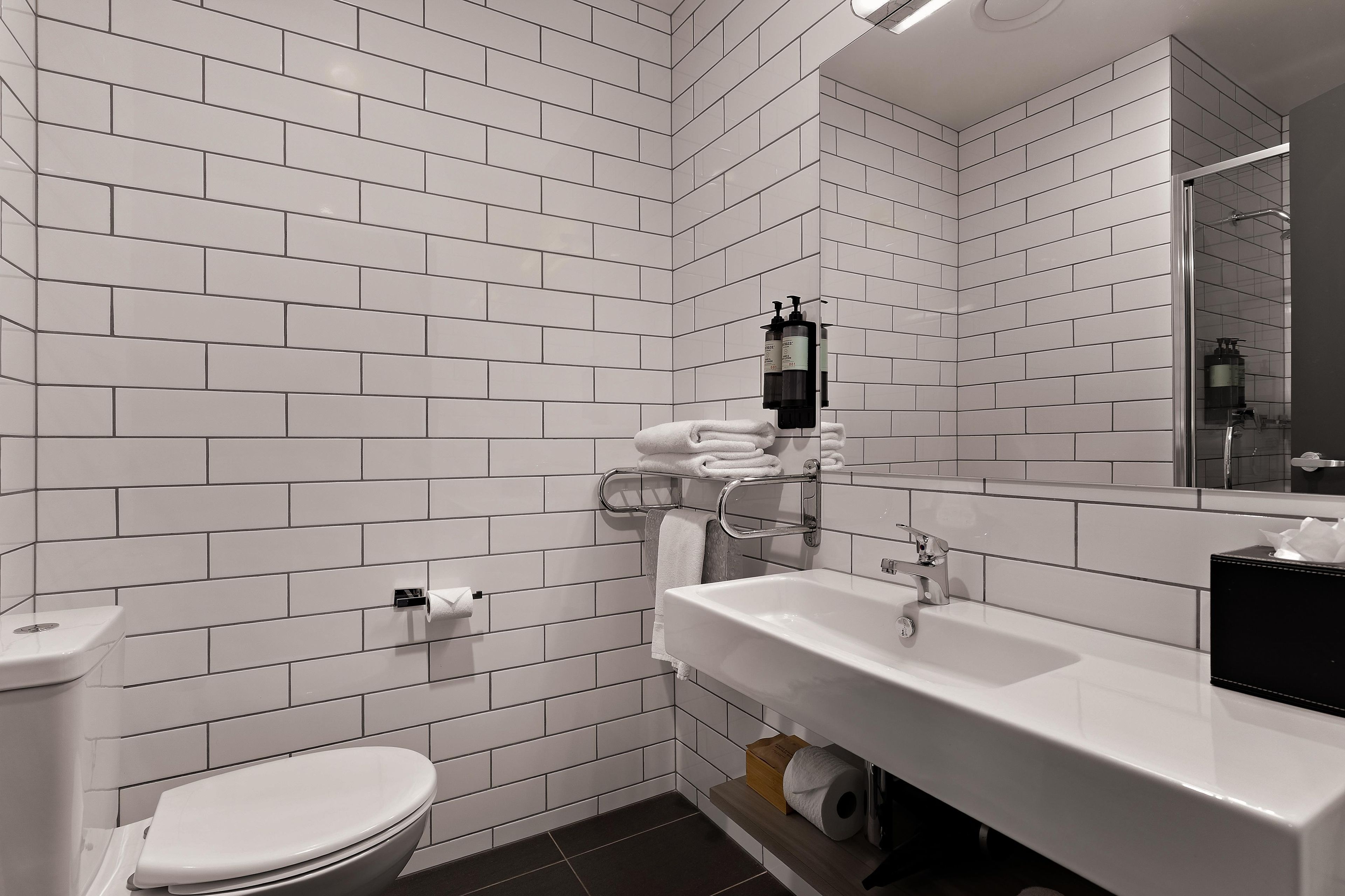 Een badkamer met witte metrotegels, een wit toilet, een wastafel met spiegel en een handdoekhouder.