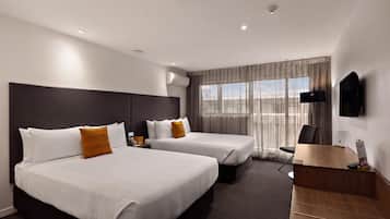 A hotel room with two beds, a desk, a chair, a TV, and a window with curtains.