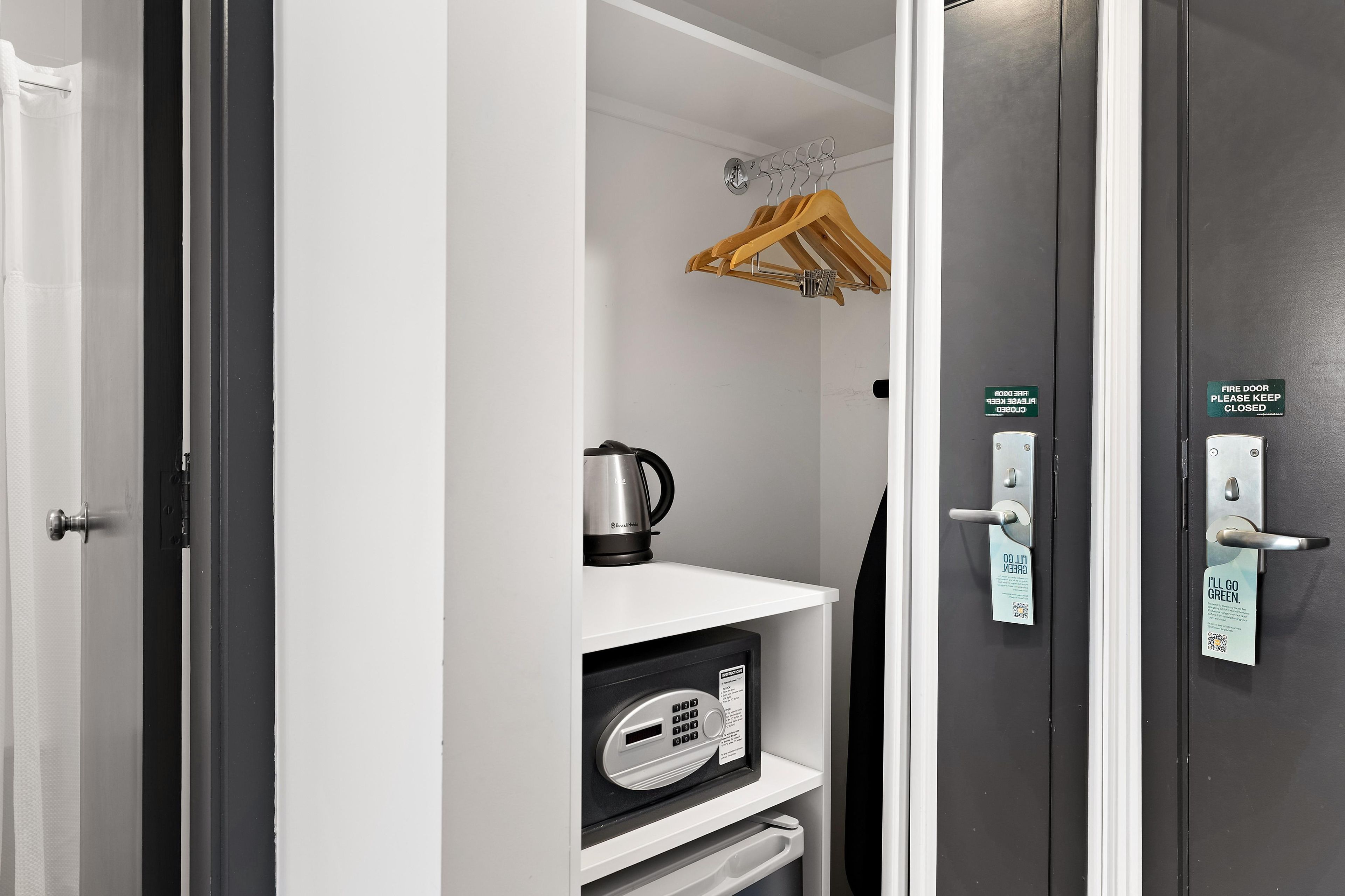 A room with a black door, a white shelf, a kettle, and a small appliance with a control panel.