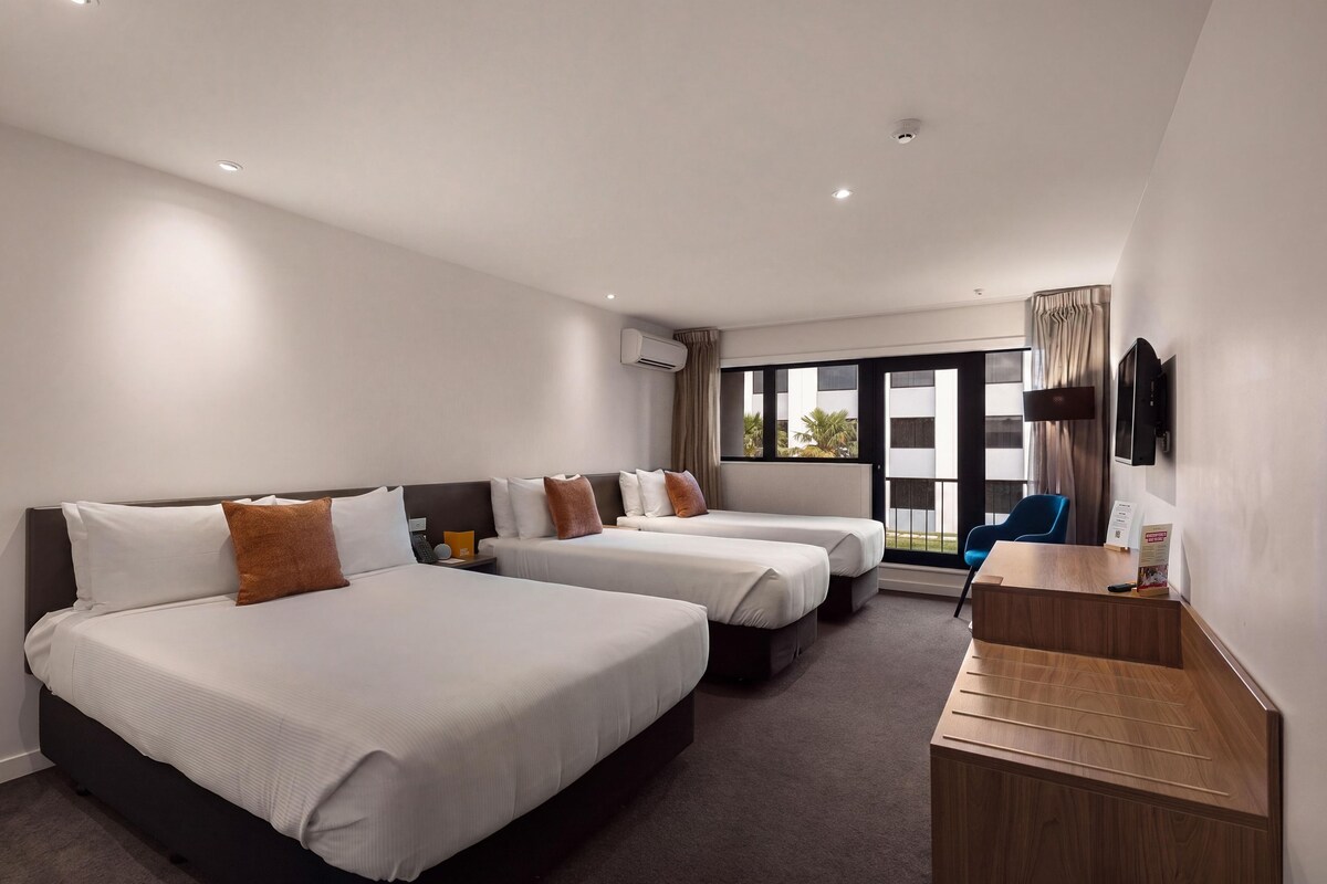 A hotel room with two beds, a desk, a TV, and a window with a view.