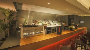 Zona de bar con una barra larga, diversas opciones de asiento y una variedad de botellas en estanterías.