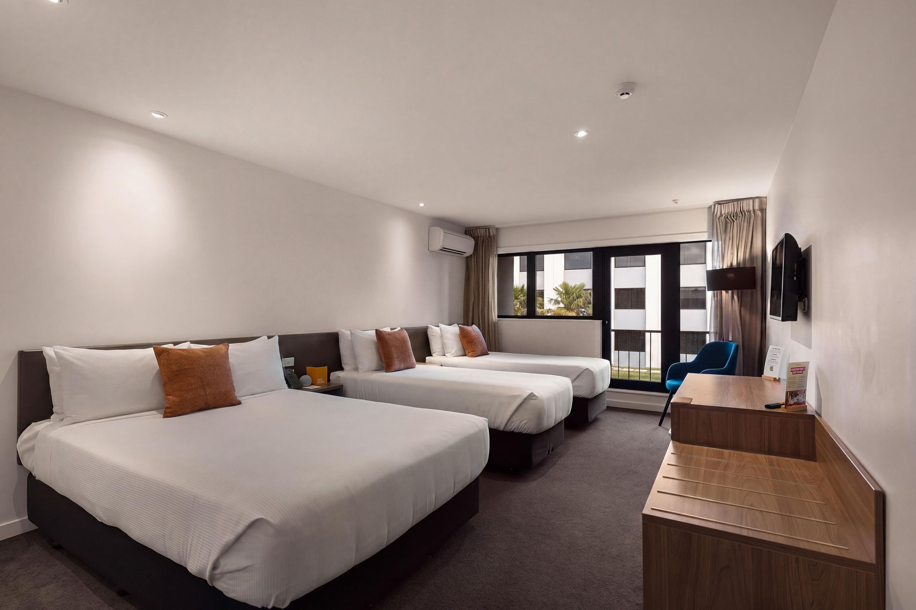A hotel room with two beds, a desk, a TV, and a window with a view.