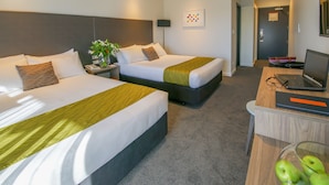 Habitación de hotel con dos camas, un escritorio con una computadora portátil y un florero con manzanas verdes.