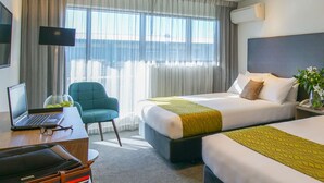 A hotel room with a bed, a desk with a laptop, a chair, and a bedside table with a vase of flowers. - Sudima Christchurch Airport (Christchurch)