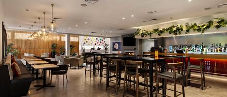 A modern bar area with a long counter, seating arrangements, and a decorative wall with circular patterns.