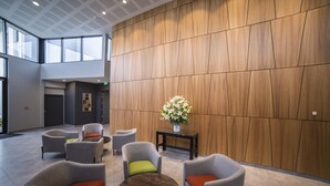 A modern lobby with grey upholstered chairs, a round wooden table, and a vase of flowers on a black side table. - Sudima Christchurch Airport (Christchurch)