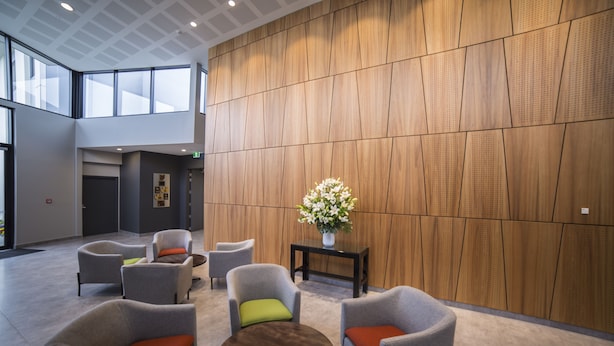 Un vestíbulo moderno con sillones tapizados en gris, una mesa redonda de madera y un jarrón de flores sobre una mesita auxiliar negra.