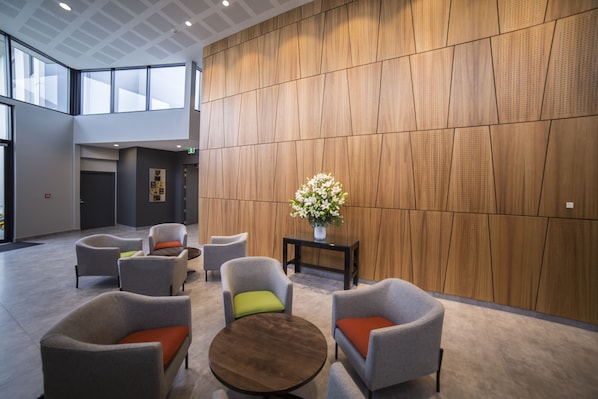 A modern lobby with grey upholstered chairs, a round wooden table, and a vase of flowers on a black side table.