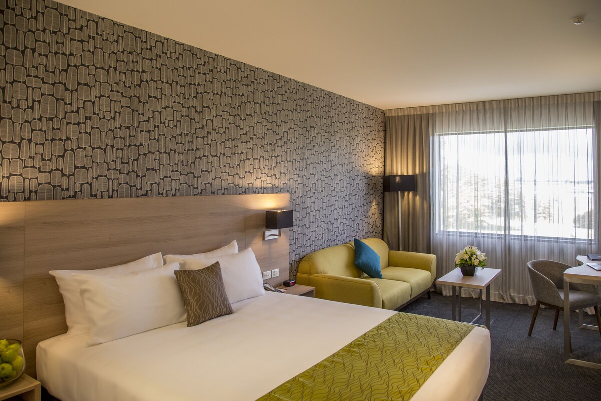 A hotel room with a large bed, a sofa, a desk, and a chair.