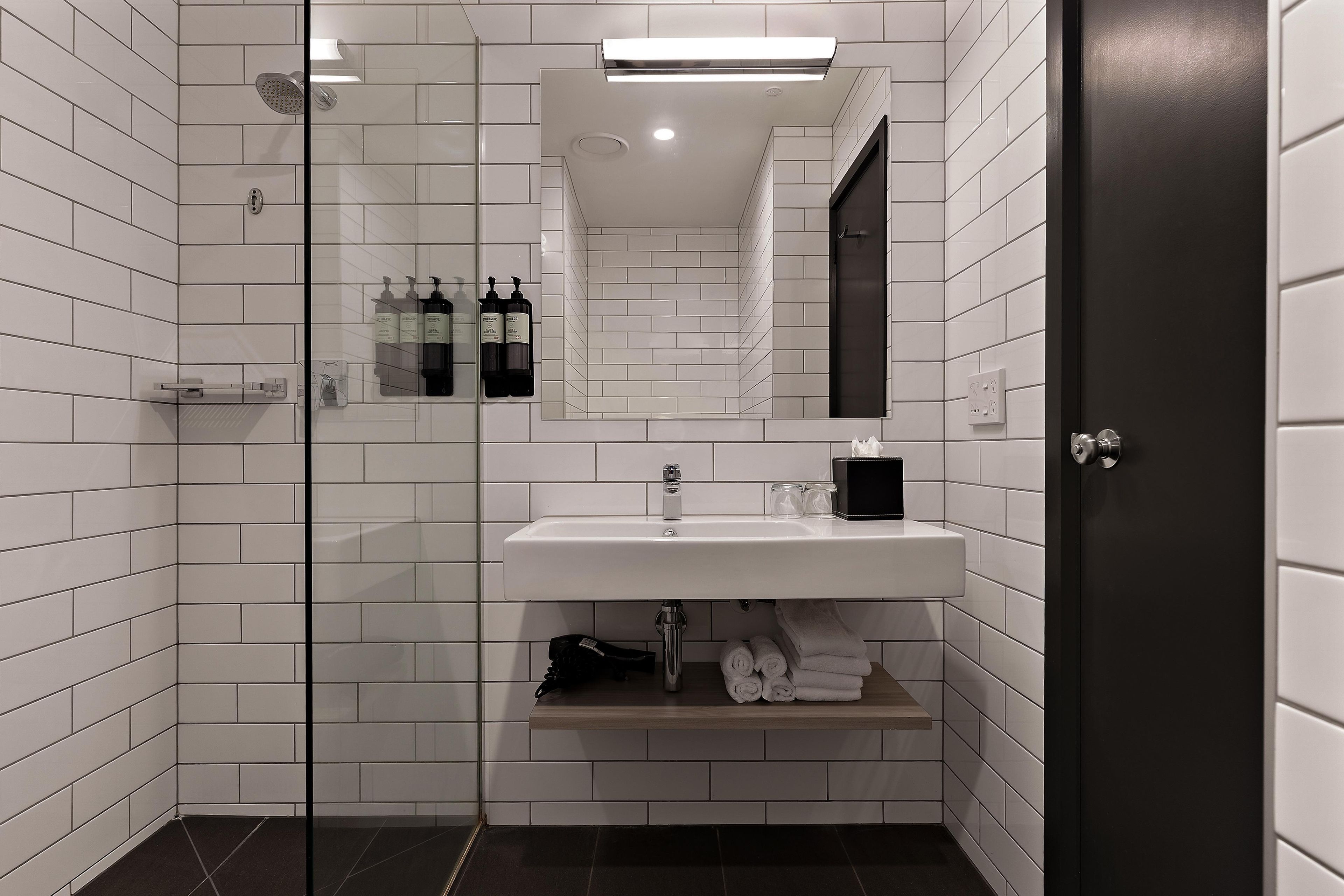 A modern bathroom with white subway tiles, a glass shower enclosure, a white sink, and a dark door.