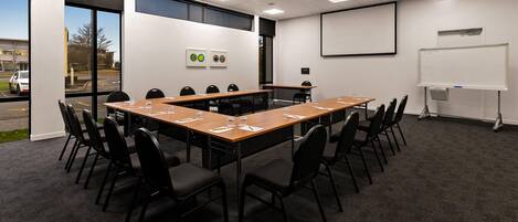 Un salón de conferencias con una larga mesa, sillas, una pantalla de proyector y una pizarra.