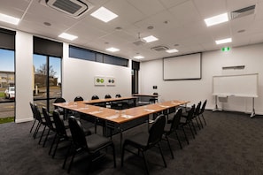 A conference room with a long table, chairs, a projector screen, and a whiteboard. - Sudima Christchurch Airport (Christchurch)