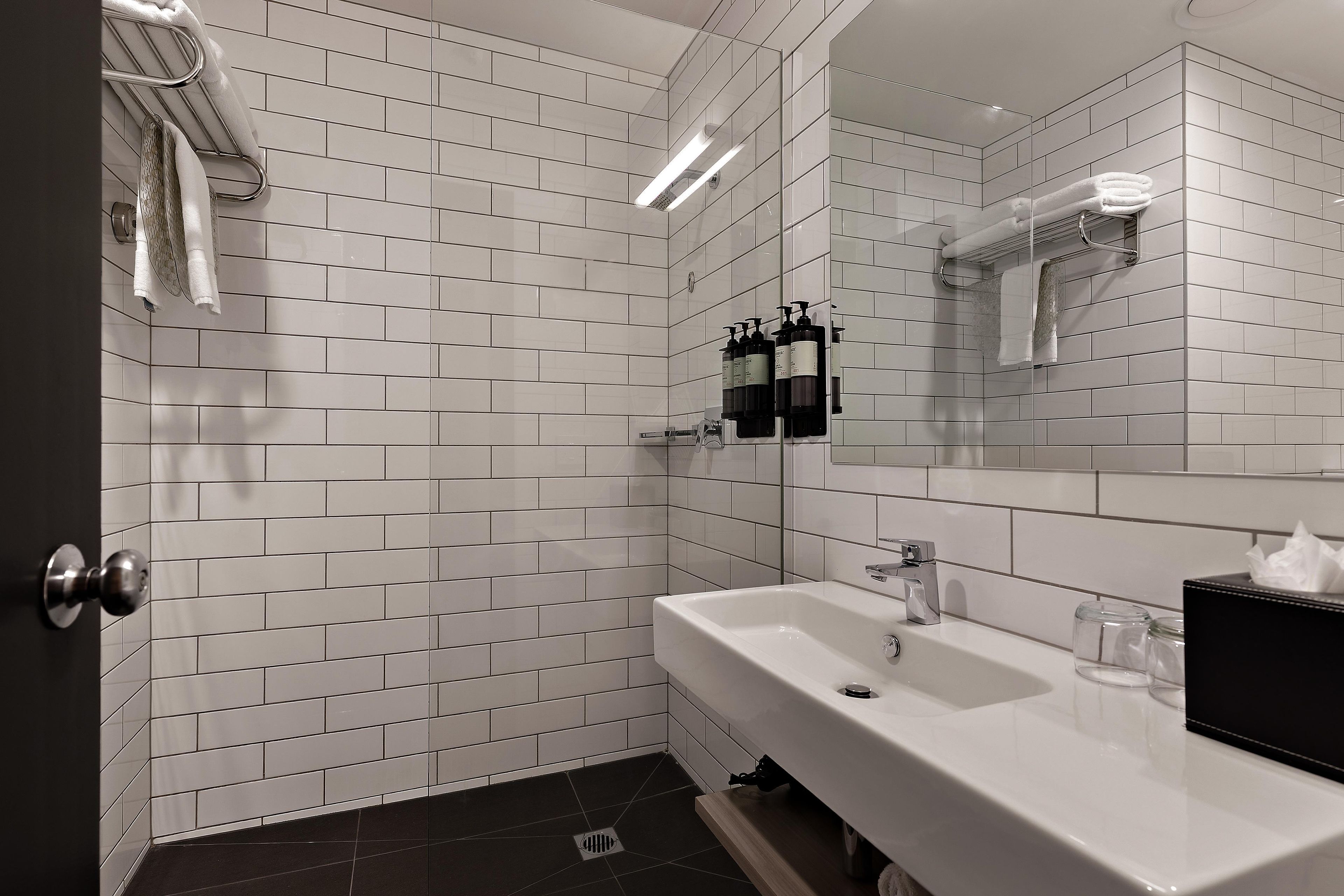 A bathroom with white subway tiles, a white sink, and a mirror.