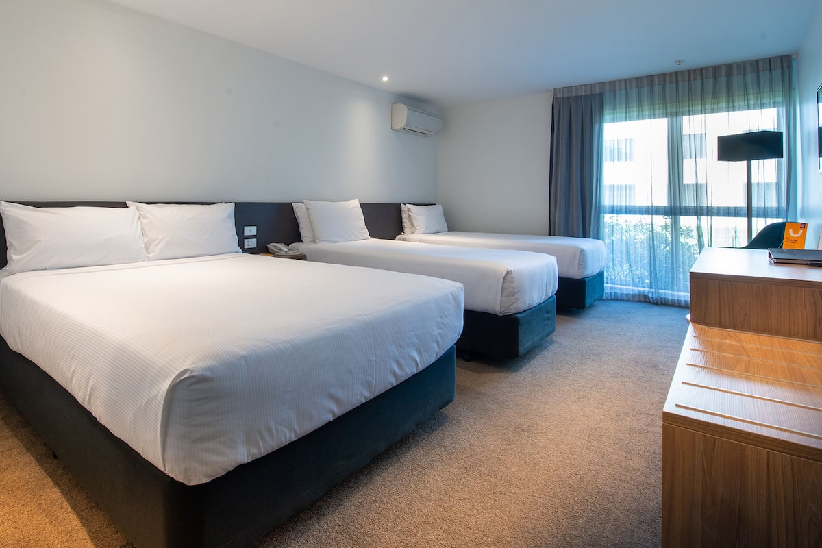 A hotel room with two beds, a desk, a chair, and a large window with curtains.
