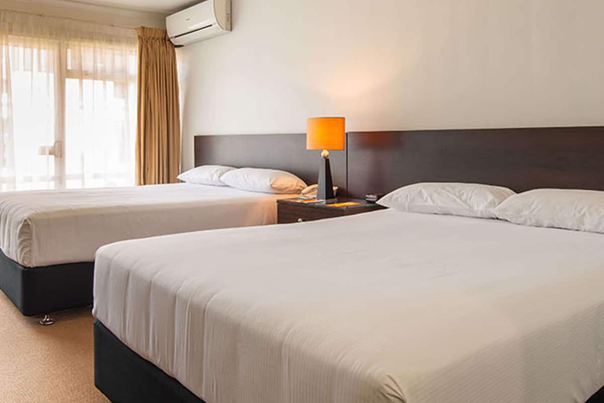 A hotel room with two beds, a nightstand with a lamp, and an air conditioning unit on the wall.