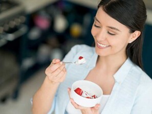 A person holding a bowl of yogurt with a spoon.