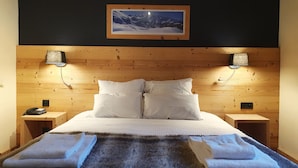 A bedroom with a wooden headboard, two bedside tables, a bed with white bedding, a mounted picture, and two wall-mounted lamps. - Chalet Hotel Du Bois (Les Houches)