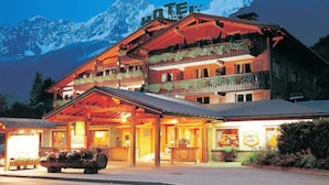A multi-story hotel with a ski resort sign, balconies with plants, and a mountain backdrop. - Chalet Hotel Du Bois (Les Houches)