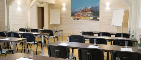 A conference room with wooden walls, tables, chairs, and a large poster of a mountain resort.