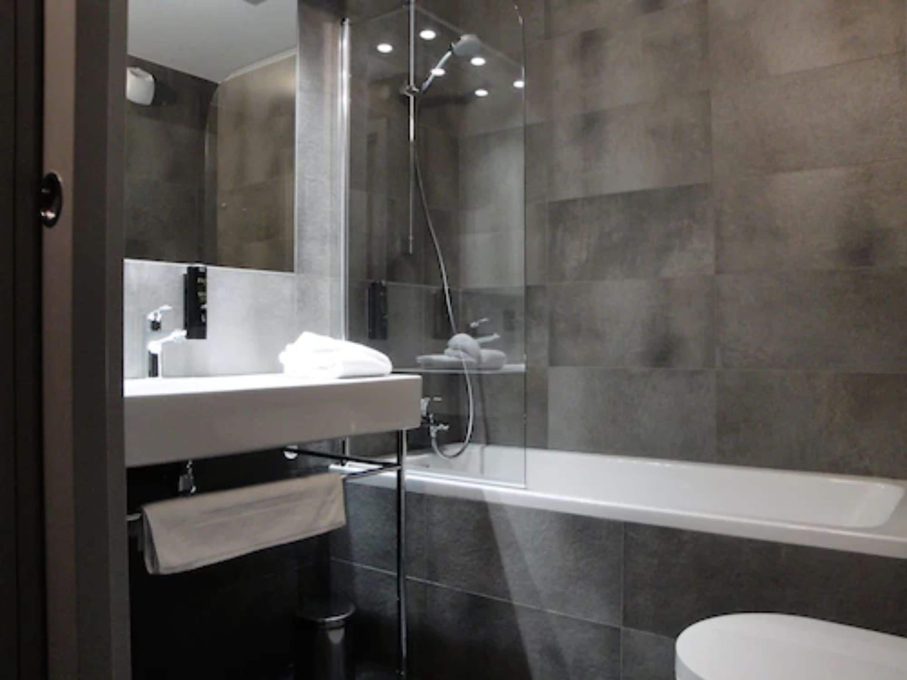 Un baño moderno con ducha de vidrio, lavamanos blanco y una bañera grande.