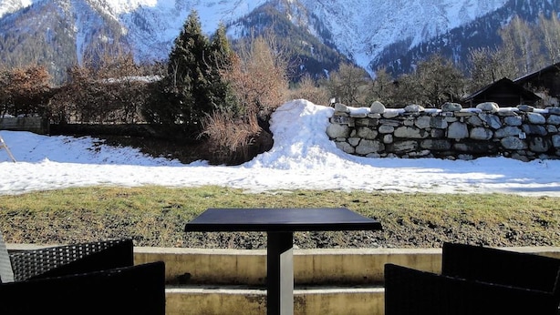 A table and chairs in a snowy outdoor setting with a stone wall and a view of snow-covered mountains. - Chalet Hotel Du Bois (Les Houches)